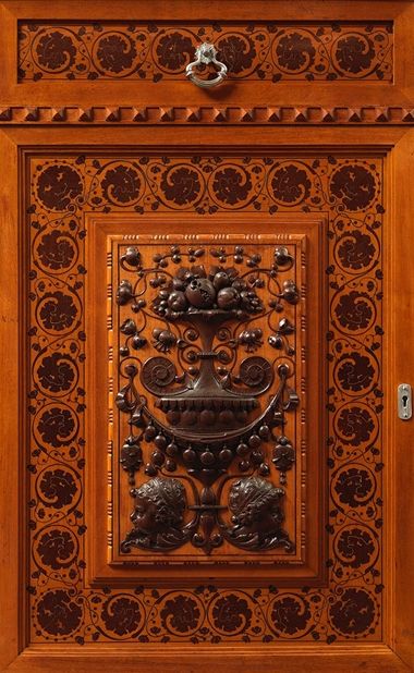 Wooden panel decorated with brass cornucopia, floral motifs, and two cherubs in profile.