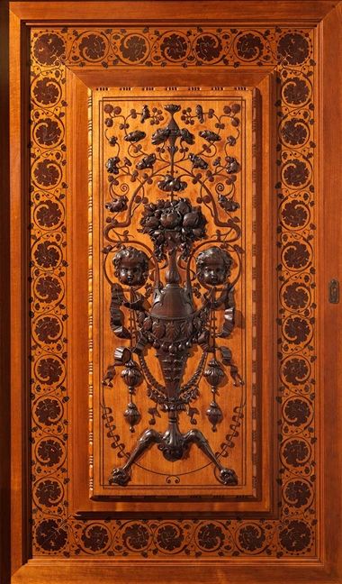 Wooden panel decorated with brass cornucopia, floral motifs, and two cherubs.