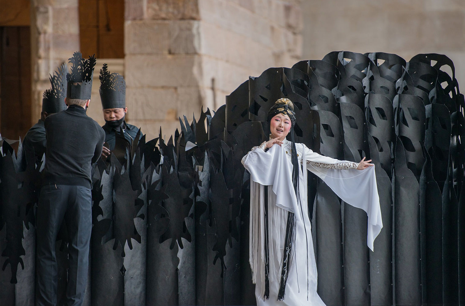 Paradise Interrupted, a poetic weaving of the Western myth of the Garden of Eden and the Chinese myth of the Peony Pavilion, performed outside of the Temple of Dendur, March 2015. An asian woman wearing a costume performing in front of a spiked black structure being held up by three men dressed in black. 