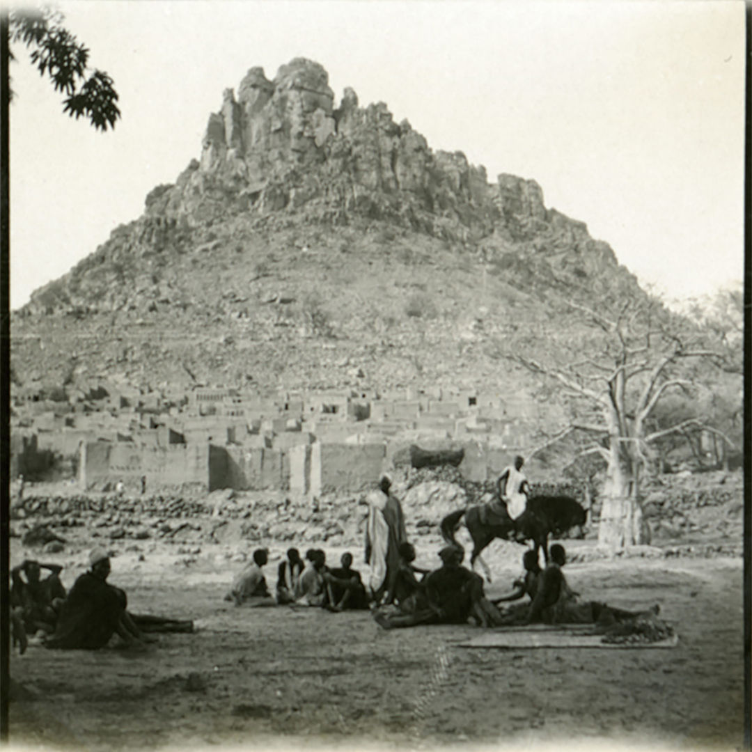 A black and white photograph of a village at the base of a mountain
